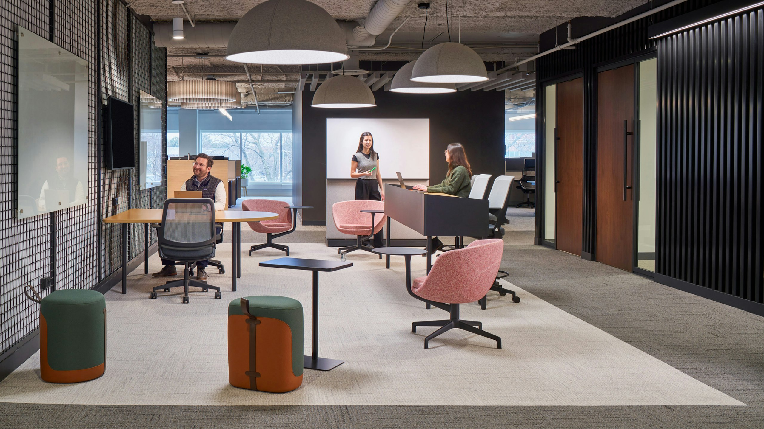 Three people working in a communal workspace furnished with Knoll Ollo chairs, pink task chairs with side tables, and a larger meeting table