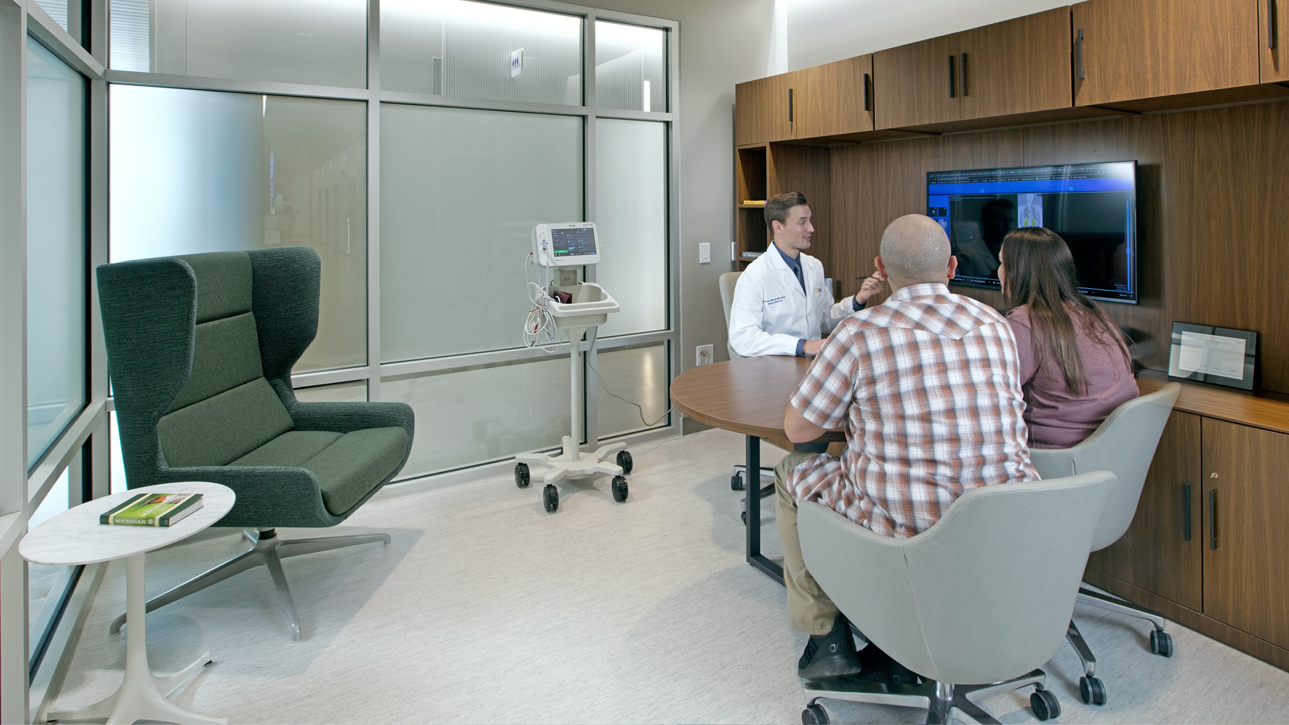 A doctor talking to two people at a table in front of a screen in a room at BAMF Health